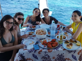 A group of friends enjoys a delicious meal aboard a boat, surrounded by stunning turquoise waters — perfect for memorable dining experiences on the water.