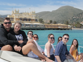 A cheerful group of friends poses on the deck of a boat, enjoying a sunny day with stunning coastal scenery in the background — perfect for memorable outings and celebrations.