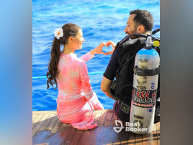 A couple shares a romantic moment by forming a heart shape with their hands while preparing for a scuba diving adventure in the beautiful ocean.