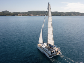 A stunning aerial view of a catamaran sailing smoothly across calm waters, surrounded by lush green hills — an ideal setting for a relaxing day on the water.