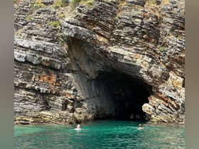 Swimmers enjoy the crystal-clear waters near a stunning cave, showcasing the natural beauty of the coastline — perfect for adventure seekers and nature lovers.