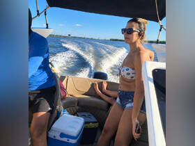 A woman enjoys a day on the water while seated on a boat, with a child’s feet visible in the background, capturing the essence of family fun and relaxation on the water.