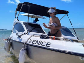 A woman stands on the deck of a boat named 'Venice' in sunny waters, enjoying a beach day — perfect for summer adventures on the water.