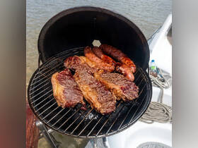 A mouthwatering display of steaks and sausages sizzling on a grill aboard a boat, perfect for a delicious barbecue experience on the water.