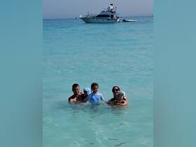 A joyful family enjoys a day in the shallow waters, with a boat anchored nearby, creating unforgettable memories under the sun.