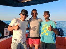 Three friends share a joyful moment on a boat, giving thumbs up against a beautiful ocean backdrop — perfect for capturing memories on the water.
