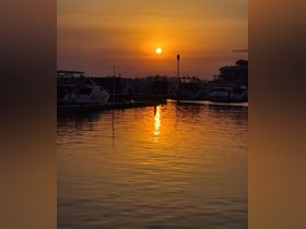 A stunning sunset reflects on the water at a marina, with boats gently docked, creating a serene atmosphere perfect for evening strolls.