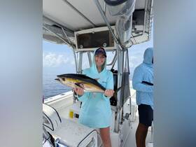 A smiling woman proudly holds her catch aboard a fishing boat, showcasing the excitement of a successful day on the water.