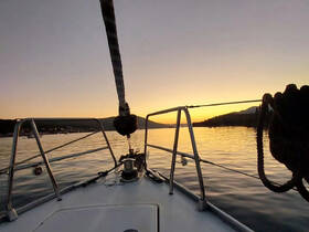 A serene sunset view from the bow of a sailboat, showcasing calm waters and a picturesque landscape — perfect for peaceful evening cruises.