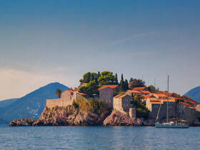 A picturesque view of a coastal island with charming stone buildings and a sailboat anchored nearby, perfect for showcasing the beauty of seaside destinations.