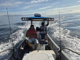 Two friends enjoy a fishing trip on a boat, navigating through calm ocean waters — a perfect day for angling and relaxation.