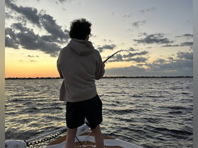 A person enjoys fishing at sunset, casting a line from the boat into the shimmering water — a perfect moment for fishing enthusiasts.