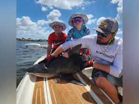 Two children and an adult interact with a shark on a boat, showcasing an exciting wildlife experience. This thrilling encounter highlights the adventure of fishing and marine life exploration.