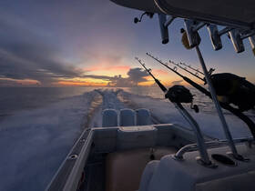 A stunning sunset view from a fishing boat, showcasing the tranquil ocean and fishing rods ready for action — perfect for anglers seeking a memorable experience on the water.