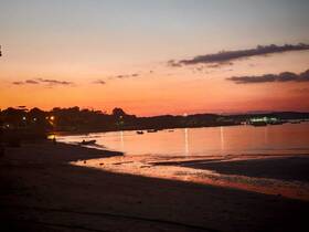 A stunning sunset casts vibrant colors over the beach, with silhouettes of people enjoying the serene coastline — a perfect moment for relaxation and reflection.