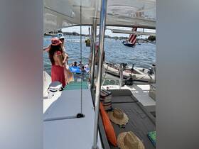 A lively group enjoys a fun day on a catamaran, with guests swimming and relaxing on the deck — perfect for summer parties and water activities.