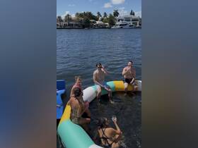 A lively group enjoys a fun day on the water, relaxing on a floating mat with cocktails in hand — perfect for summer parties and celebrations.