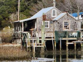 A rustic waterfront structure partially obscured by vegetation, showcasing a unique architectural style typical of coastal regions.