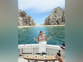 A woman poses playfully on the deck of a boat, surrounded by stunning rock formations and clear waters, capturing the essence of a fun day on the water.