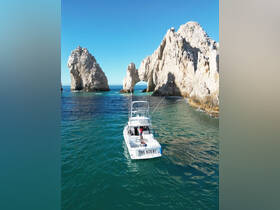 A scenic view of 'The Hobby' boat navigating near the iconic rock formations of Cabo San Lucas, showcasing the stunning ocean backdrop.