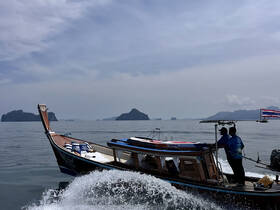 A traditional longtail boat speeds through tranquil waters, showcasing stunning island scenery — perfect for exploring the beauty of coastal destinations.