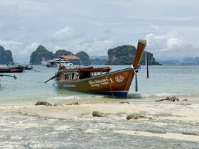 A traditional longtail boat is docked on a sandy beach, surrounded by stunning limestone cliffs and clear waters, perfect for exploring the beautiful coastline.