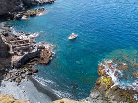 An aerial view captures a boat navigating along a stunning coastline, showcasing the beautiful turquoise waters and rocky shores — perfect for exploring hidden gems.