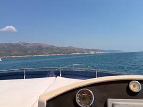 A scenic view from the bow of a boat cruising along a beautiful coastline, showcasing the clear blue waters and distant hills.