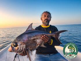 A proud angler holds up a large fish against a stunning sunset backdrop, showcasing the thrill of fishing in the Maldives.