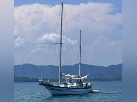 A beautiful sailboat navigates through calm waters, showcasing its elegant design against a backdrop of lush mountains.