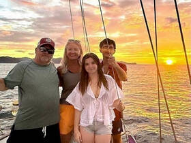 A joyful group poses for a photo on a sailboat at sunset, capturing a memorable sailing experience with stunning views.