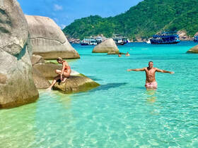 Two people enjoy a sunny day at the beach, with one swimming in the clear turquoise water and the other relaxing on a rock — a perfect tropical getaway.