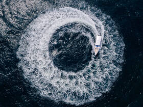 An aerial view of a boat making a sharp turn, creating a stunning circular wake in the water — a thrilling moment captured on the open sea.