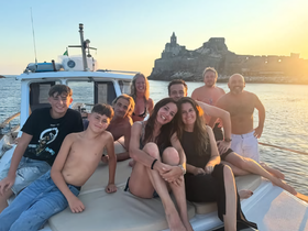 A joyful group of friends and family poses on a boat at sunset, capturing a memorable moment against a stunning coastal backdrop.