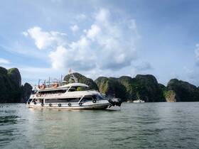A stunning yacht navigates through serene waters, surrounded by lush green cliffs, showcasing the beauty of the landscape.
