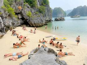 A vibrant beach scene with groups of people sunbathing and swimming in the clear waters, showcasing the perfect getaway for relaxation and fun in the sun.