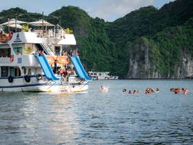 A lively scene of guests enjoying water activities, with some swimming and others preparing to slide down from the boat — perfect for a fun day on the water.