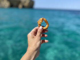A hand holds a delicious snack against a stunning turquoise backdrop, perfect for enjoying while on a boat trip.