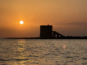 A stunning sunset casts a golden glow over a historic tower by the water, creating a picturesque scene perfect for romantic evenings or scenic boat tours.