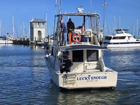 The fishing boat 'Lucky Enough' is docked at a marina with crew members preparing for departure, showcasing a vibrant day on the water.