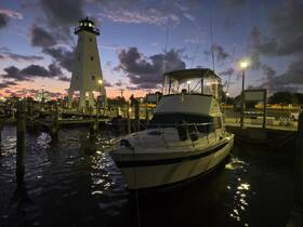 A serene view of a yacht docked at sunset, with a lighthouse in the background, creating a picturesque marina scene.