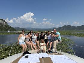 A lively group of friends enjoys a sunny day on the water, posing on the bow of a boat surrounded by beautiful scenery and lily pads — perfect for memorable outings and celebrations.