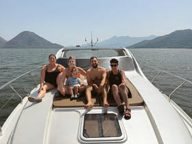 A joyful family enjoys a sunny day on a boat, capturing a moment of relaxation and togetherness against a scenic backdrop of mountains and water.