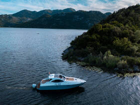 Aerial view of a sleek yacht available for rent, gliding through serene waters surrounded by lush hills — perfect for exploring the scenic coastline.