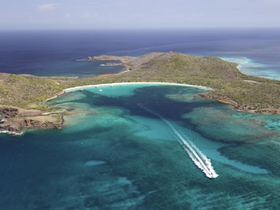 A stunning aerial view of a picturesque island coastline with turquoise waters and a boat cruising through the clear sea, perfect for showcasing tropical destinations.