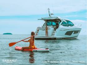 A woman paddleboards in the foreground while another enjoys the sun on the deck of the luxurious Lady M Sunseek 2020 yacht, showcasing a perfect day of water activities and relaxation.