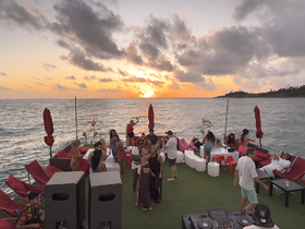 A vibrant group enjoys a sunset party on a yacht, complete with music and drinks, creating the perfect atmosphere for celebration on the water.