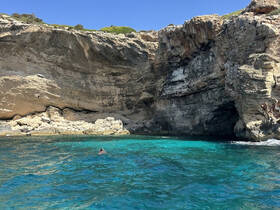 A swimmer enjoys the clear turquoise waters near a stunning rocky cave, showcasing the beauty of the coastline and perfect for adventurous outings.