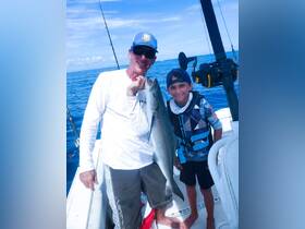 A joyful moment captured as a man and a child proudly display their catch while fishing on the open ocean — a perfect family adventure on the water.