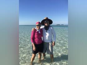 A cheerful couple enjoys a sunny day at the beach, standing in shallow water with a beautiful island backdrop — perfect for memorable island adventures.